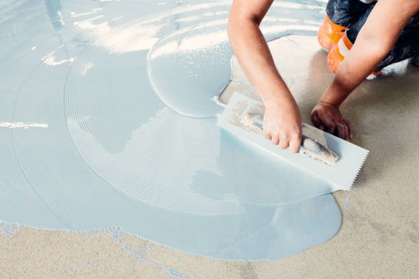 Construction worker carefully spreading self-leveling concrete mixture on the floor using a trowel to create a perfectly smooth surface