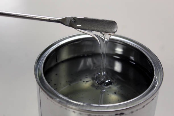 Technician weighing transparent epoxy resin for a paint in a can on a balance by spatula on white background