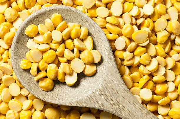 A wooden spoonful of chana dal  peas resting on a pile of beans